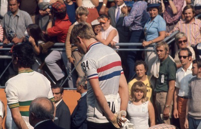 Hennie Kuiper buigt op het erepodium deemoedig het hoofd nadat hem het Olympisch goud is omgehangen. Rechts de nummer drie, de Spanjaard Jaime Huélamo, die na een positieve dopingtest zal worden gediskwalificeerd. Voor de volksliederen draaien Kuiper en zilveren Clyde Sefton een kwartslag (foto onder), waardoor het ineens lijkt alsof de Australiër links van Hennie staat.