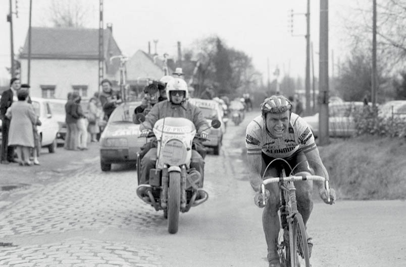 Hennie Kuiper has distanced himself from the competition, but in the background mechanic Gilbert Cattoir is not yet at ease. He hangs out of the car preventively to be able to intervene. This is difficult because Kuiper's spare bike is in the middle of the roof. Cattoir wants to switch the bikes around, but team manager Fred De Bruyne reassures: 'We're almost there...'