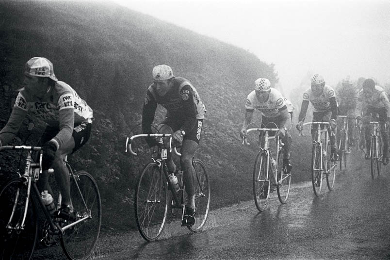 The top of the Tourmalet is shrouded in mist. A ghostly group with Lucien Van Impe, Joop Zoetemelk, and Hennie Kuiper at the front bravely faces the fog.