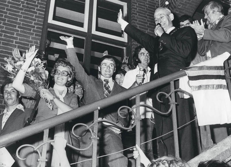 Op de trappen van het gemeentehuis van Ossendrecht wordt Hennie Kuiper toegesproken door burgemeester André van Gils (rechts) en toegejuicht door de plaatselijke bevolking. Rechts naast Kuiper is het hoofd van zijn moeder Johanna nog net te zien. Rechts naast haar VARA’s Dingen van de dag-verslaggever Frits Bom