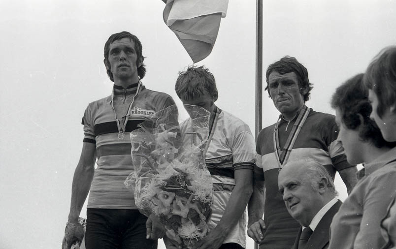 De teleurstelling druipt niet, maar spoelt van het WK-podium in Yvoir. Terwijl wereldkampioen Hennie Kuiper luistert naar het Wilhelmus, heeft Roger De Vlaeminck (links) de blik gericht op een punt voorbij oneindig en door het hoofd van Jean-Pierre Danguillaume (rechts) speelt kennelijk ook nog steeds een heel ander scenario