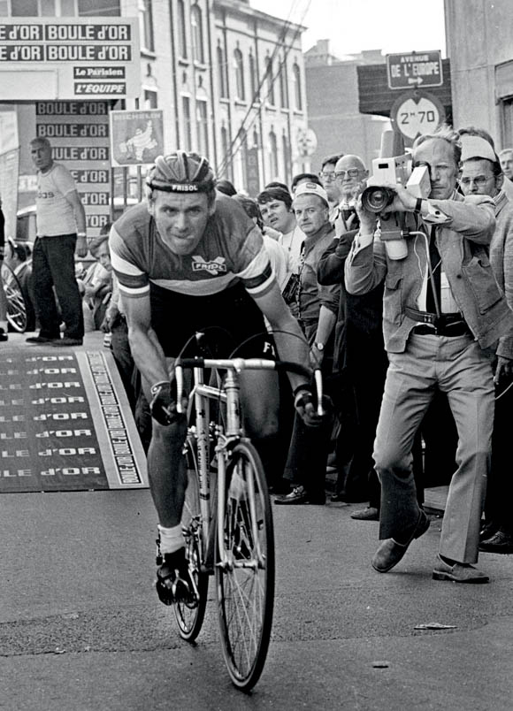 On June 26, 1975, Hennie Kuiper - tongue out of his mouth - starts the prologue of the Tour de France with great concentration. The cameraman on the right is struggling to capture Hennie well in his shot. Francesco Moser wins the race against the clock over 6.2 kilometers. Hennie finishes very commendably in tenth place.