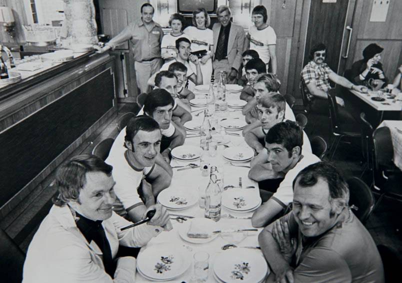 The Frisol team at the table in Charleroi at the start of the 1975 Tour de France. Left at the table, from front to back: sponsor Nico de Vries (with pipe!), Theo Smit, Gerard Kamper, Ben Koken, José De Cauwer and Fedor den Hertog. Right at the table from front to back: team manager Piet Libregts, Cees Priem, Hennie Kuiper, Henk Prinsen, Australian Don Allan and Portuguese Fernando Mendes