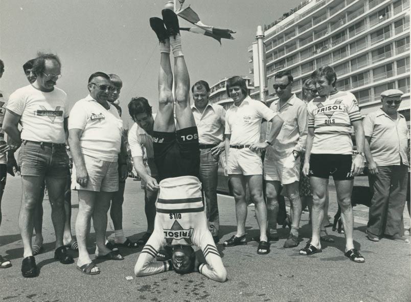 The well-known pose of Fedor den Hertog: he stands on his head. Hennie Kuiper is half hidden behind assistant team manager Edgard De Maere. To the left of De Maere, caregiver Lambert Toebak beams. Caregiver Rudy Bergmans, specially hired for Fedor, keeps Fedor's Frisol shirt in place. To the right of Fedor, team manager Piet Libregts and all the way to the right José De Cauwer.