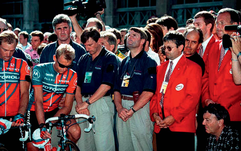 In Pau, a minute of silence is held for Fabio Casartelli. Hennie Kuiper has his gaze directed towards the sky. All the way to the right, UCI jury member Wim Jeremiasse bites his lip. To the right of Hennie, Paul Sherwen bows his head and Alain Bondue stares into the endless distance. Casartelli's teammates are Canadian Steve Bauer and New Zealander Stephen Swart, who wear a black armband as a sign of mourning.